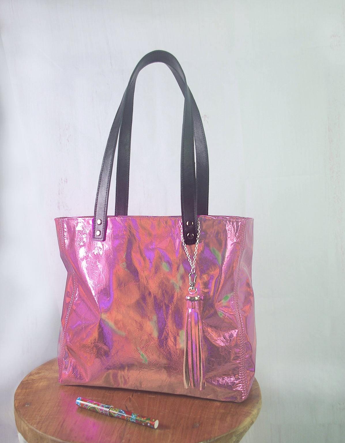Holographic pink handbag on a wooden stool with a white background