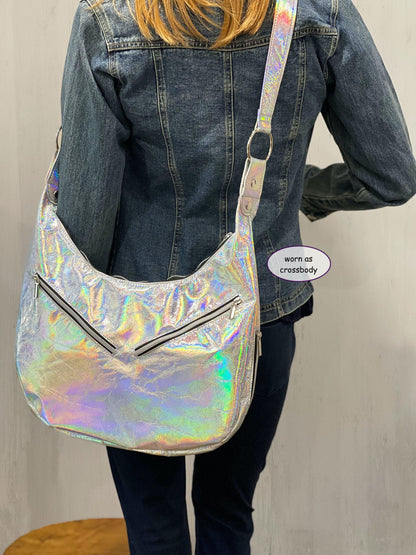 Person wearing a holographic silver hobo worn as crossbody bag with a plain background