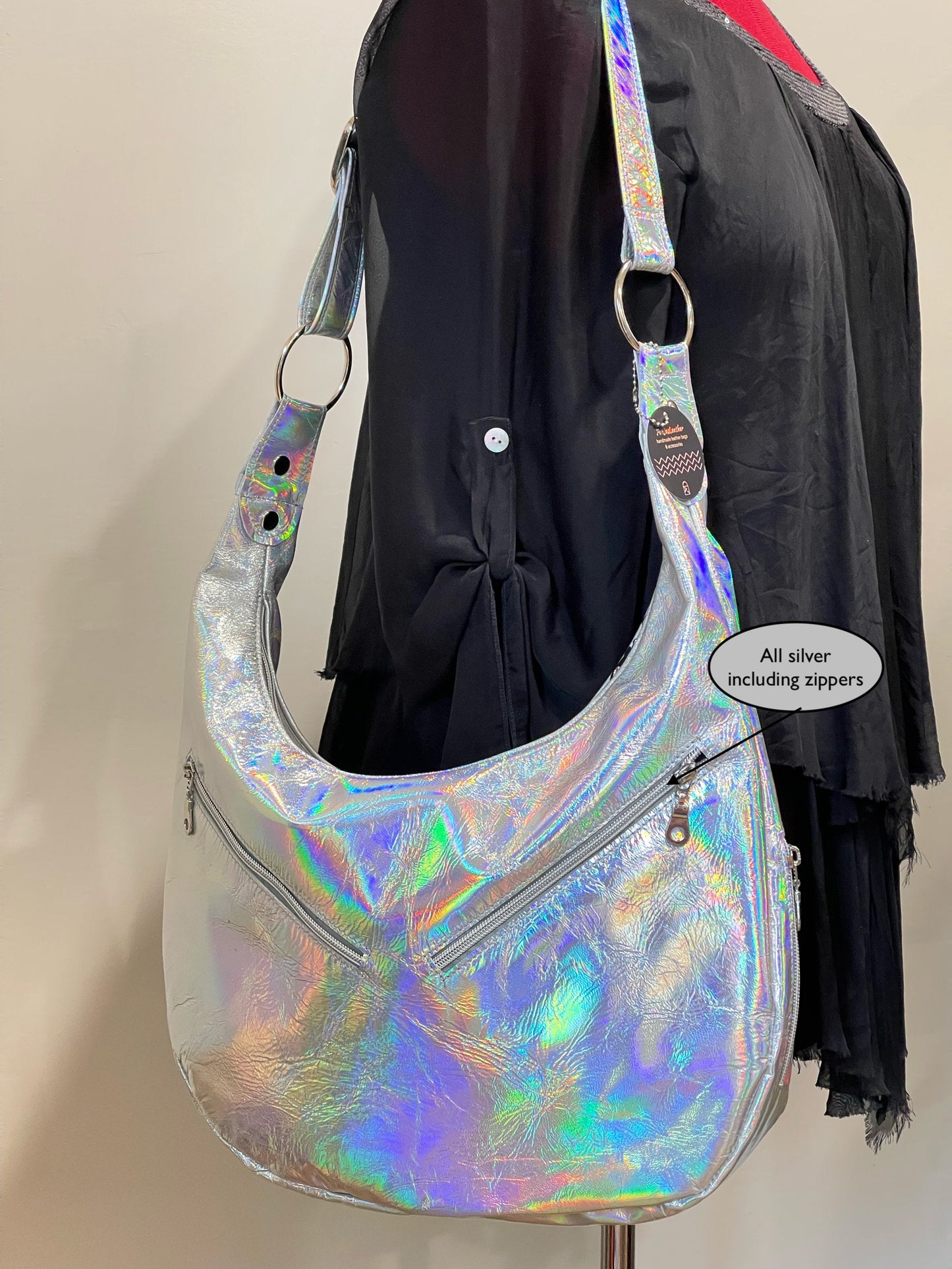 Holographic handbag with a rounded bottom and silver hardware on the shoulder of a model with black silk blouse on a beige background