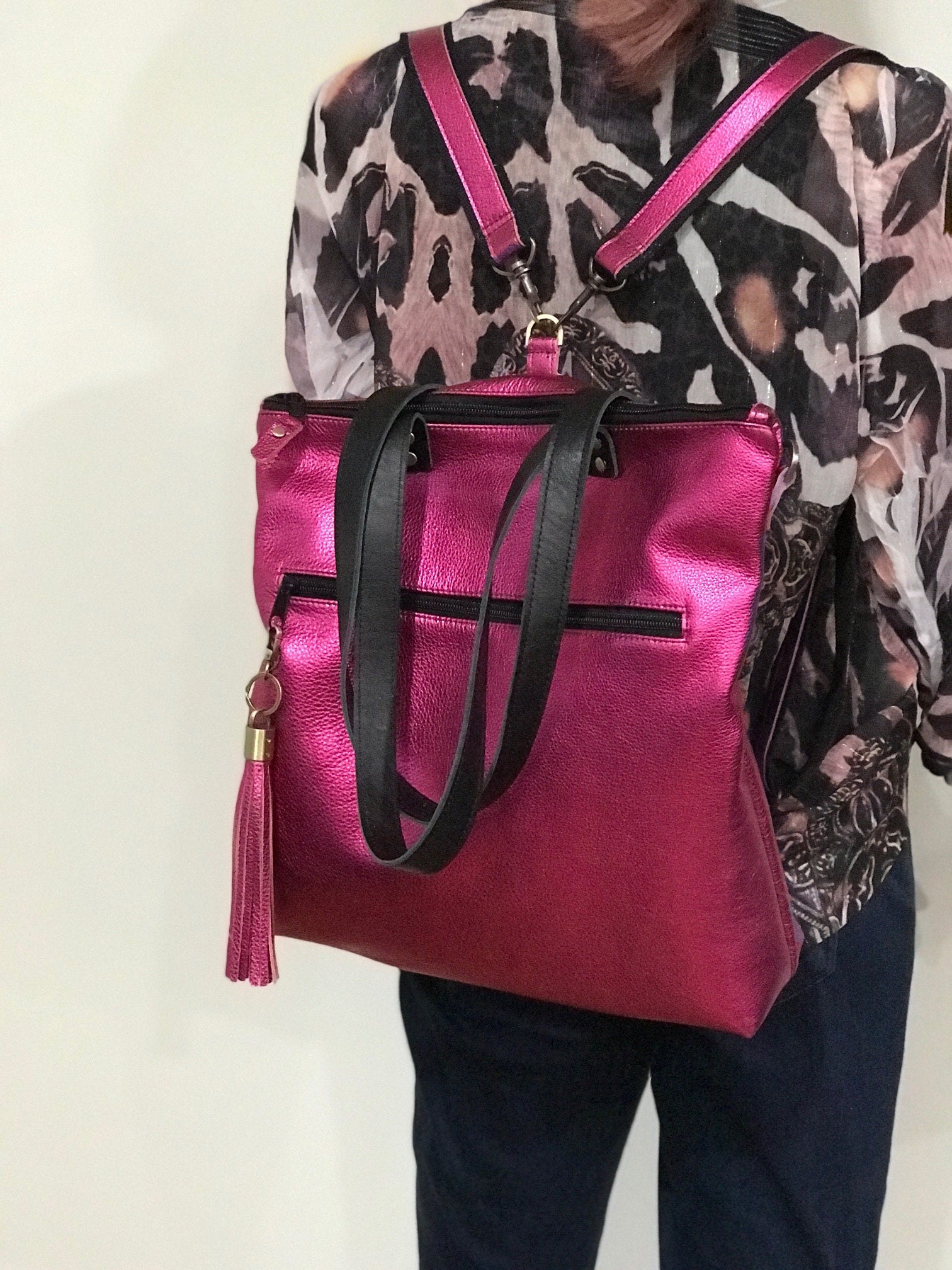 Person with a pink backpack and black tote handles against a neutral background