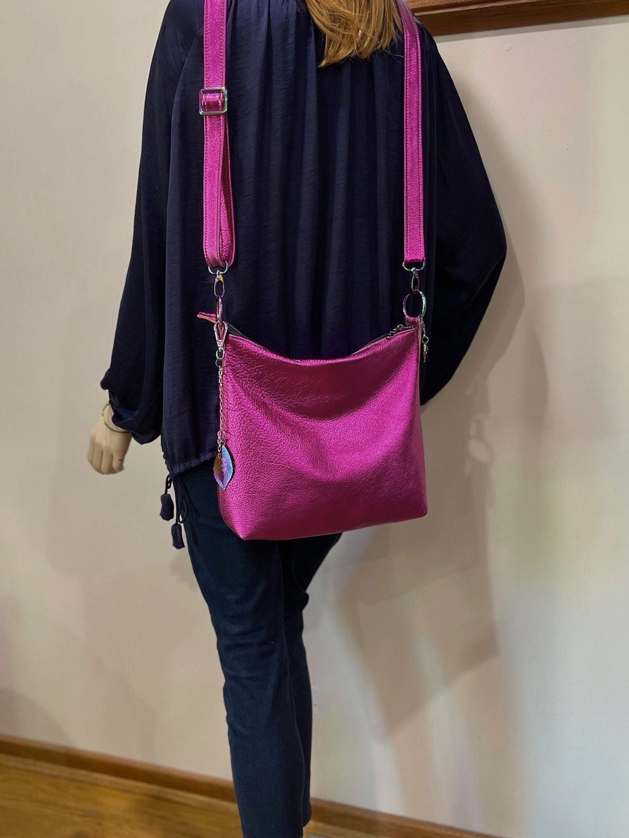 Person wearing a navy silk blouse and jeans with a bright pink shoulder bag against a plain wall.