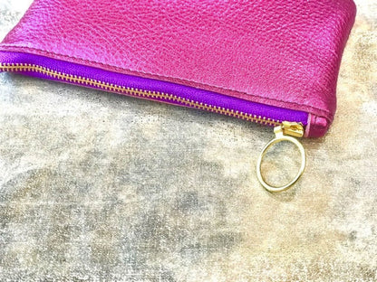 Pink leather pouch with purple zipper on a textured surface