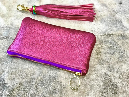 Pink leather wallet with purple zipper and matching tassel on a textured surface