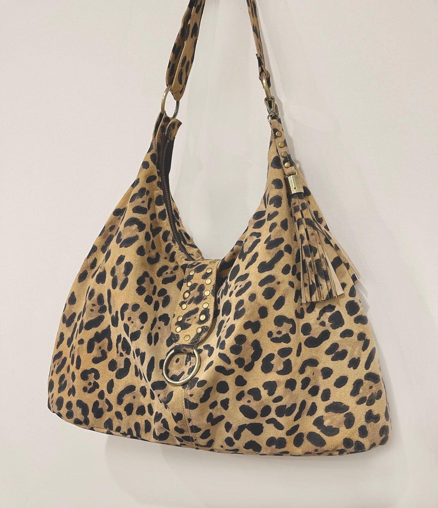 Leopard print handbag with a gold ring attached to a small flap on a light gray background