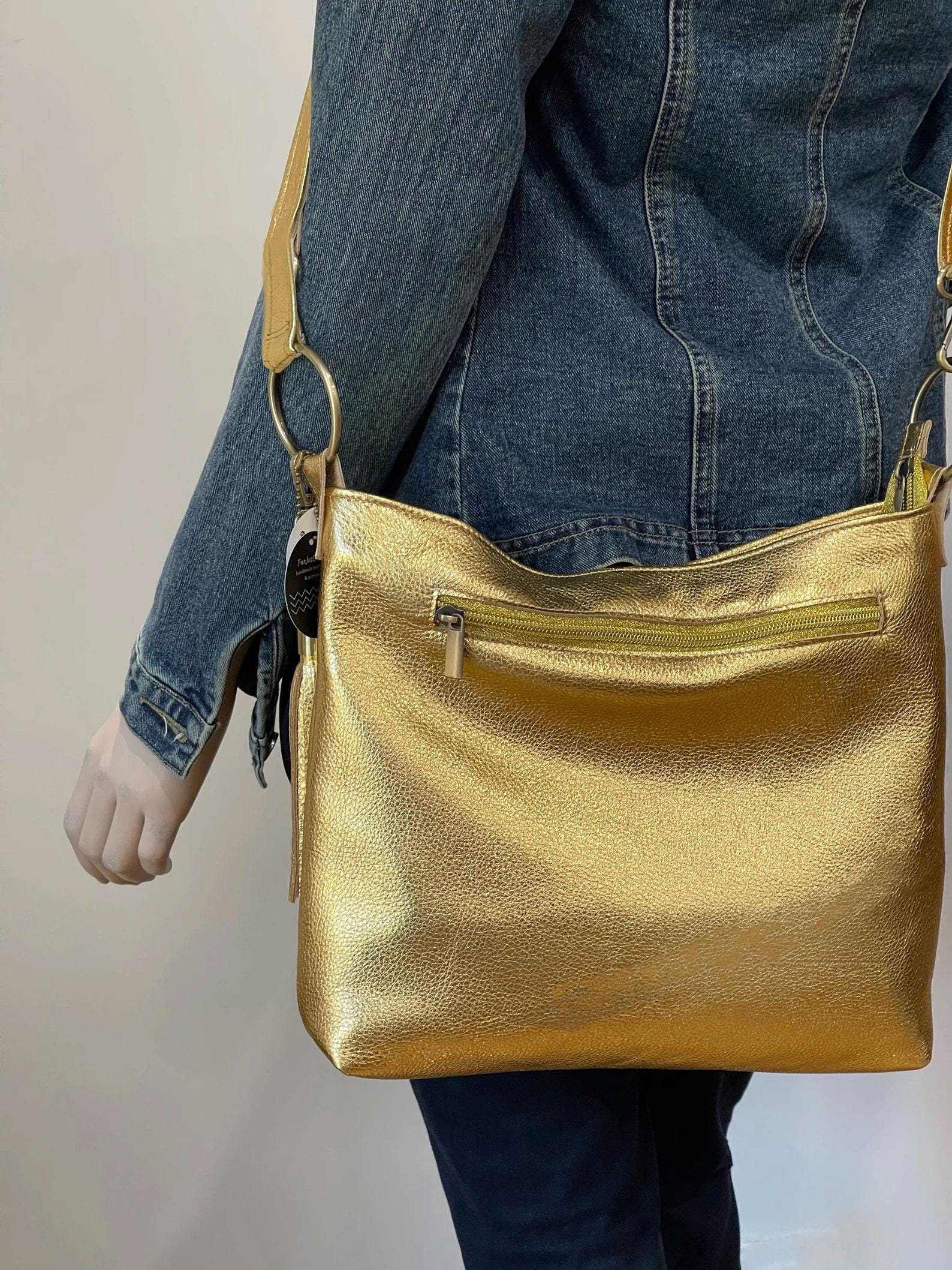 Gold handbag with a deep ziper pocket worn by a person with a neutral background