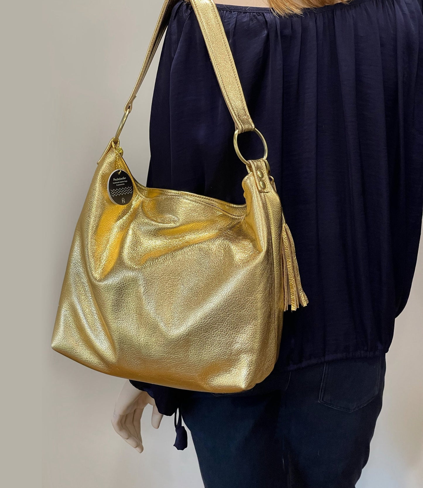 Gold handbag with tassel held by a person wearing a dark outfit against a neutral background