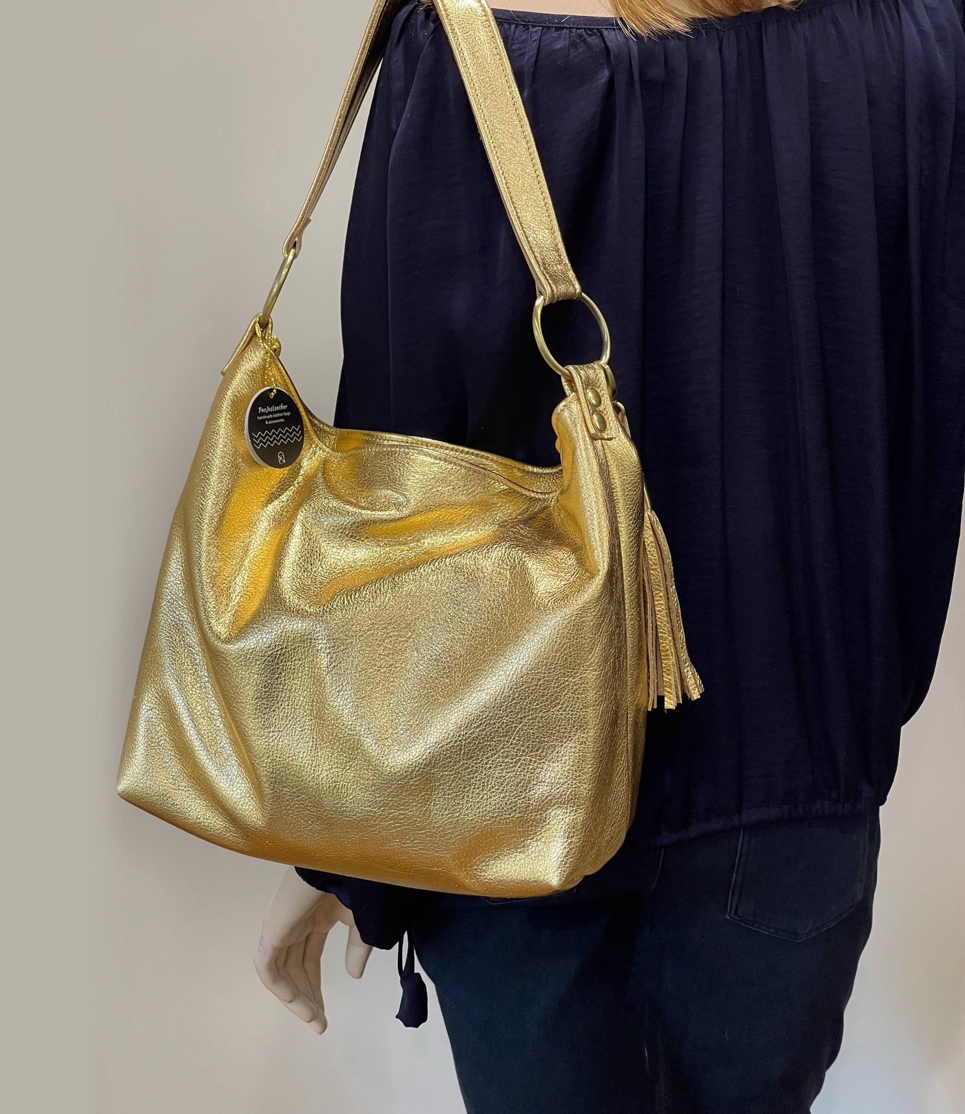 Gold handbag with tassel held by a person wearing a dark outfit against a neutral background