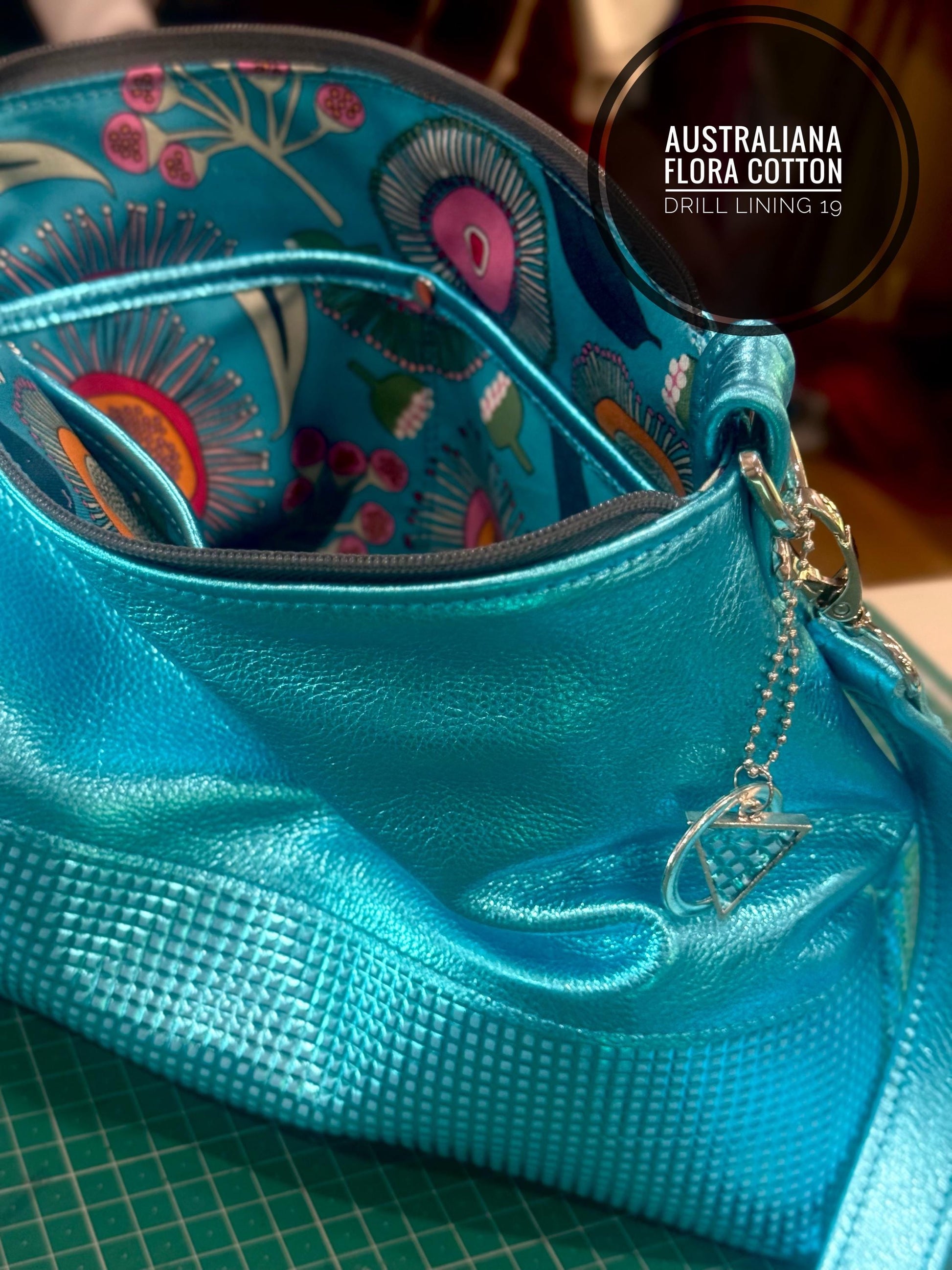 turquoise metallic Blue bag open that shows floral lining Australian Flora Cotton. A bag charm in matching metal and textured leather hangs off bag