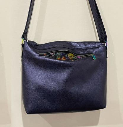 Navy blue leather handbag with floral pattern on a beige background
