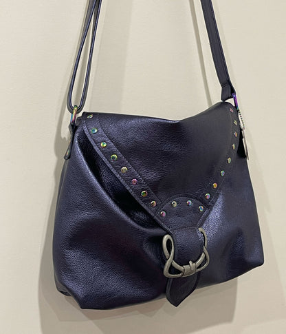 Navy blue leather handbag with decorative studs and celtic buckle on flap on a beige background