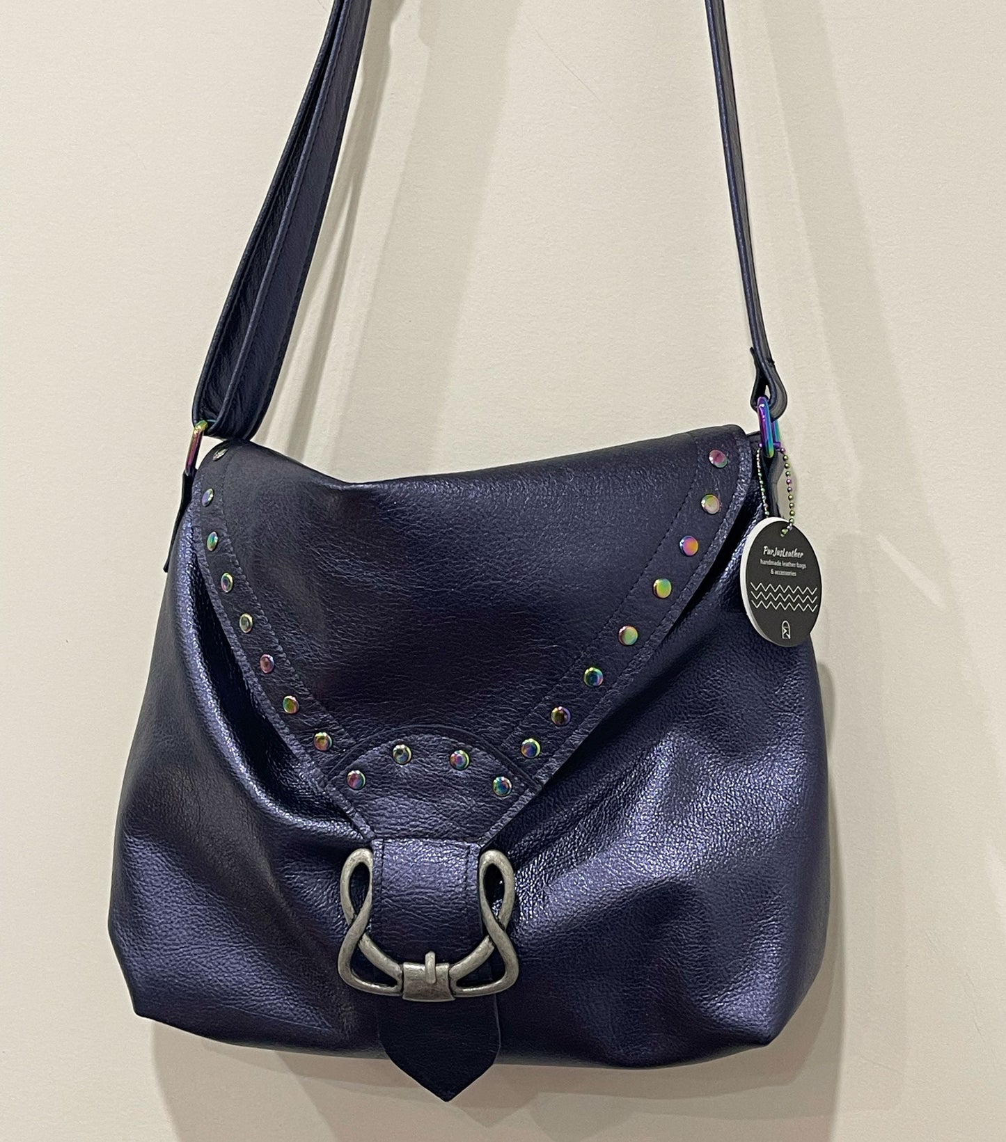 Navy blue leather handbag with decorative studs and a silver buckle on a beige background