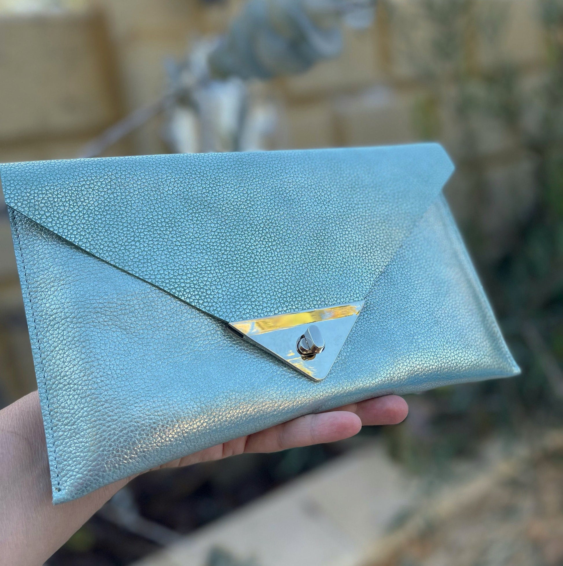 Light Turquoise blue clutch held by a hand with unique rectangle turn clasp