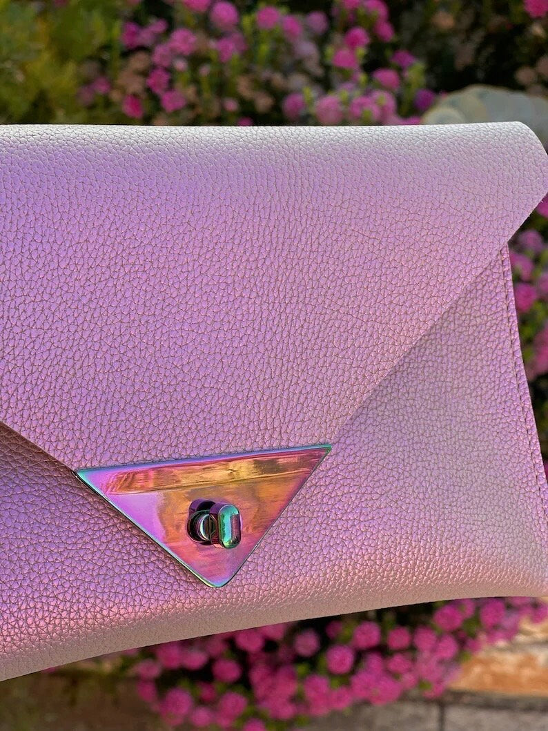 Pink clutch bag with a metallic triangle clasp against a blurred floral background