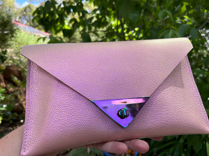 Pink clutch bag with a reflective purple triangle held in front of a green, leafy background