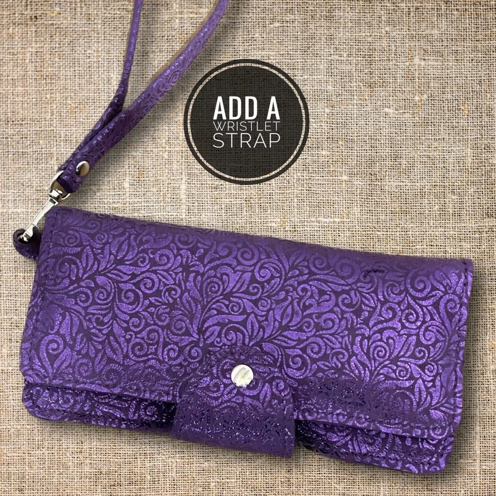 Purple pattern on purple clutch with wristlet strap on a textured beige background