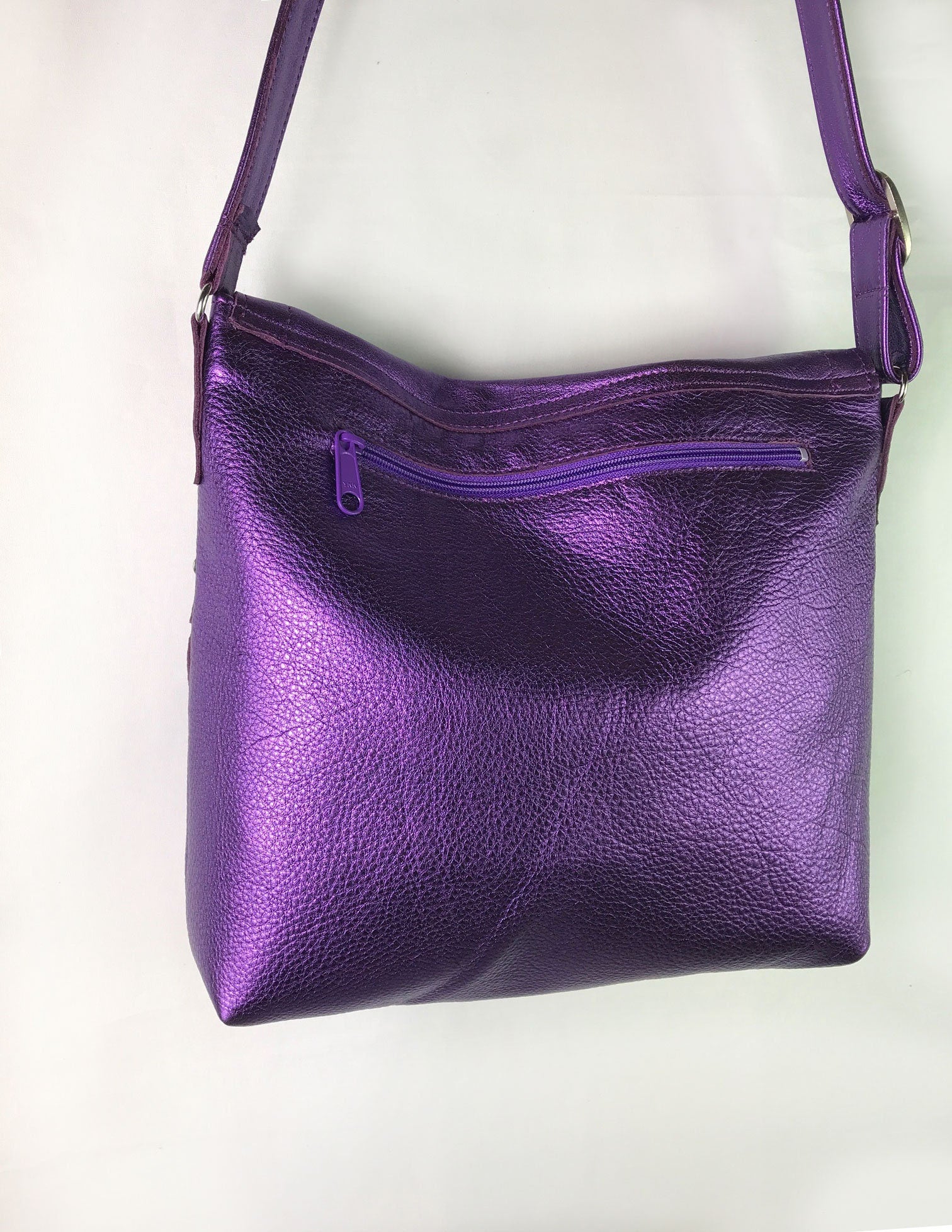 Back side of Purple leather handbag with a zipper pocket and a shoulder strap on a white background