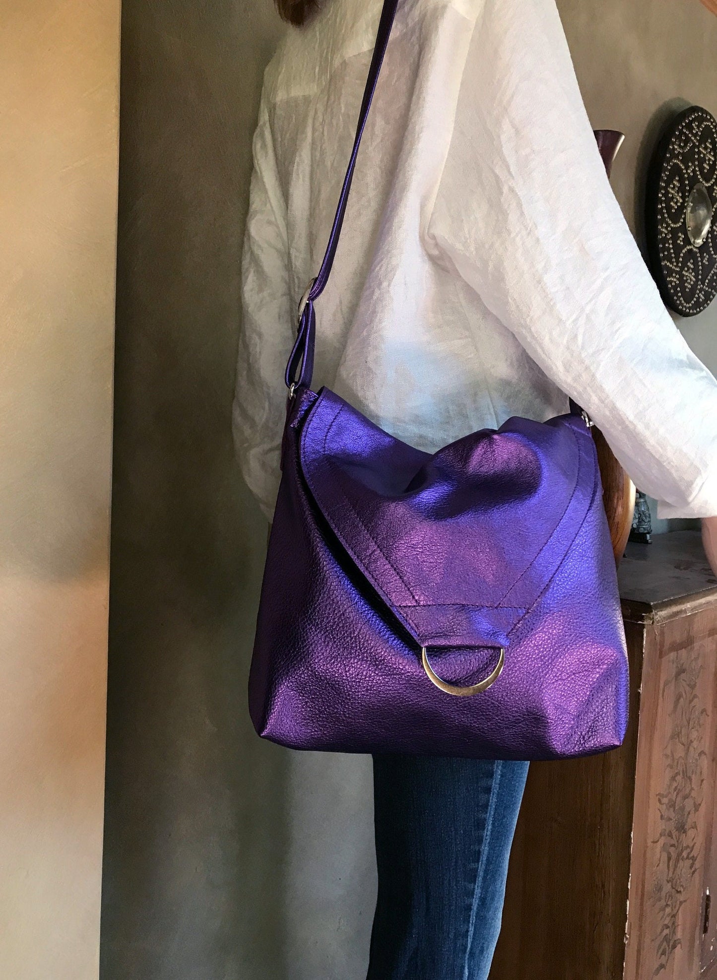Person holding a purple handbag with flap and metal ring, model wearing jeans and white blouse