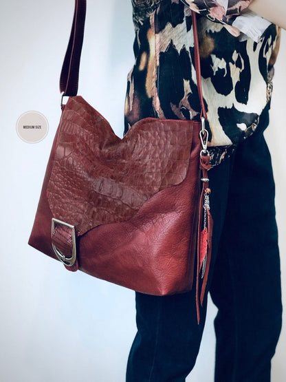 burgundy leather handbag with a person wearing a patterned top and dark pants on a white background