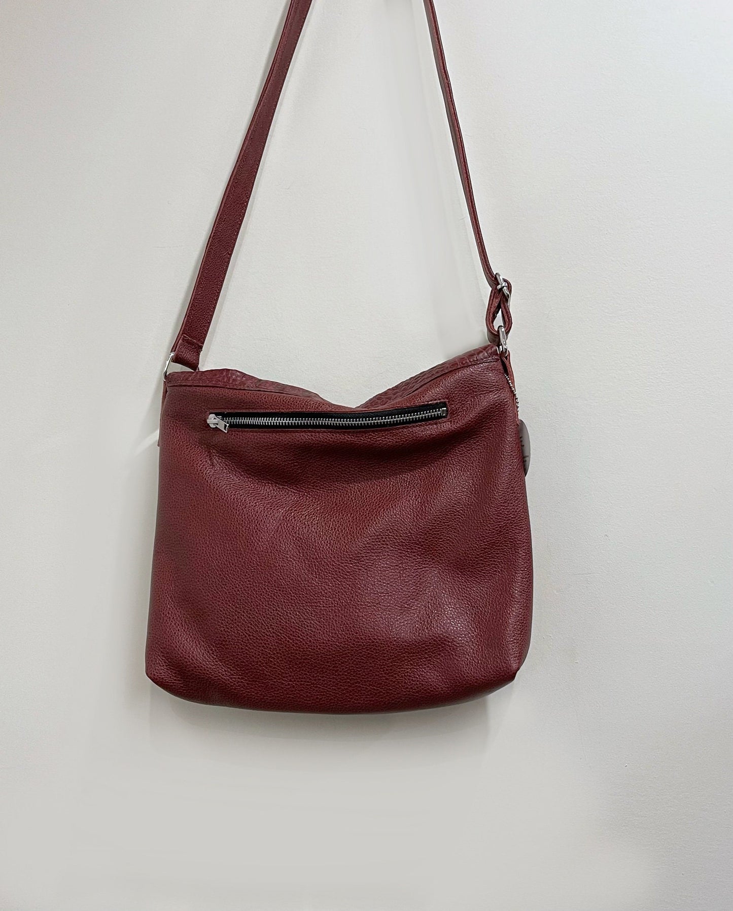 Maroon leather handbag with a visible zipper on a light gray background