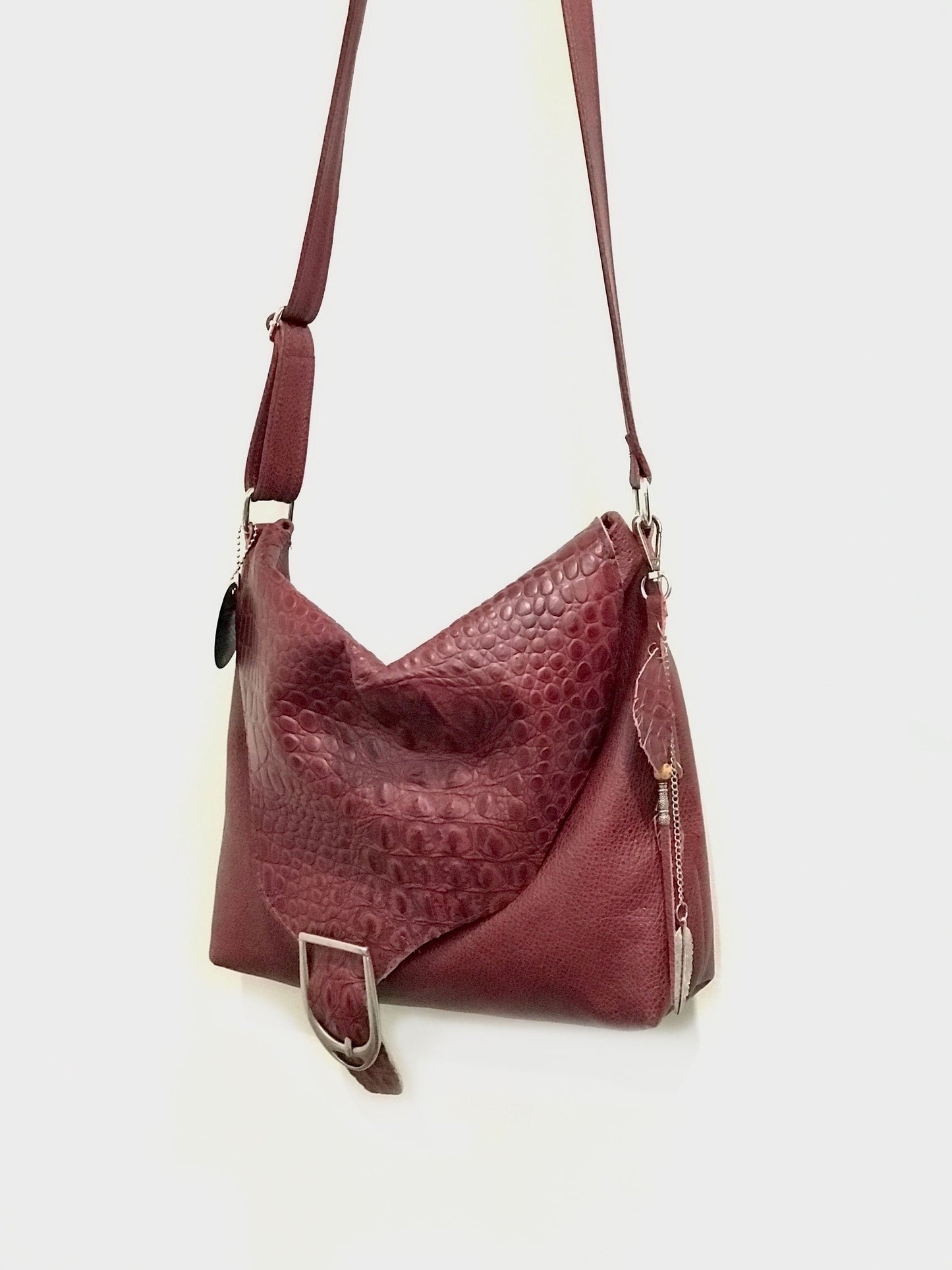 Maroon leather handbag with a textured pattern and bag charm on a white background