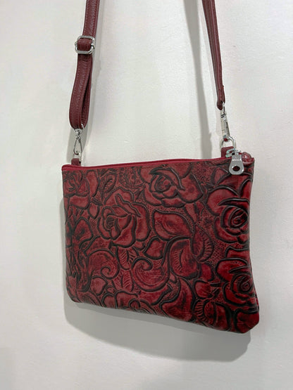 Red leather handbag with floral tooled pattern and narrow leather strap removable and adjustable on a white background