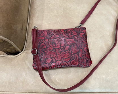 Red leather handbag with floral pattern on a beige surface