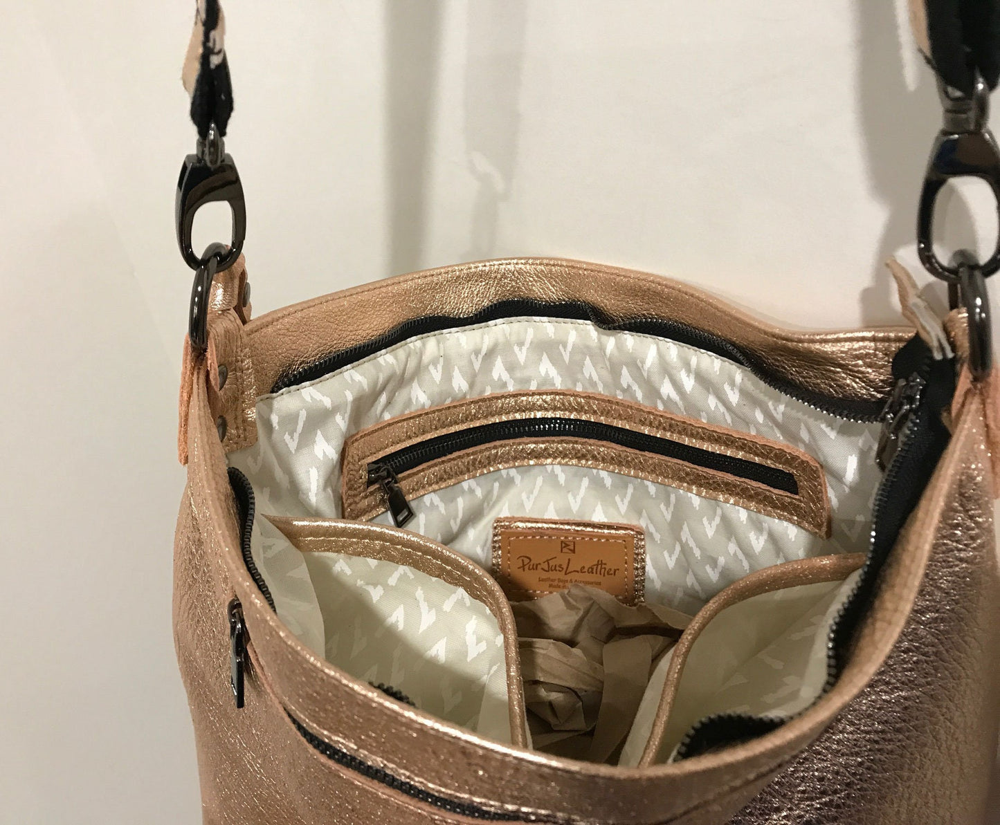 Close-up of a rose gold metallic handbag with the inside showing a zipper pocket and 2 slip pockets and zipper closure