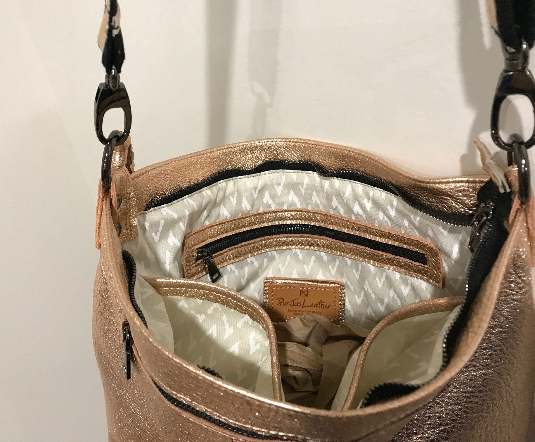 Close-up of a rose gold metallic handbag with the inside showing a zipper pocket and 2 slip pockets and zipper closure