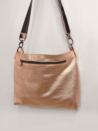 Rose gold handbag with a black zipper on a light gray background