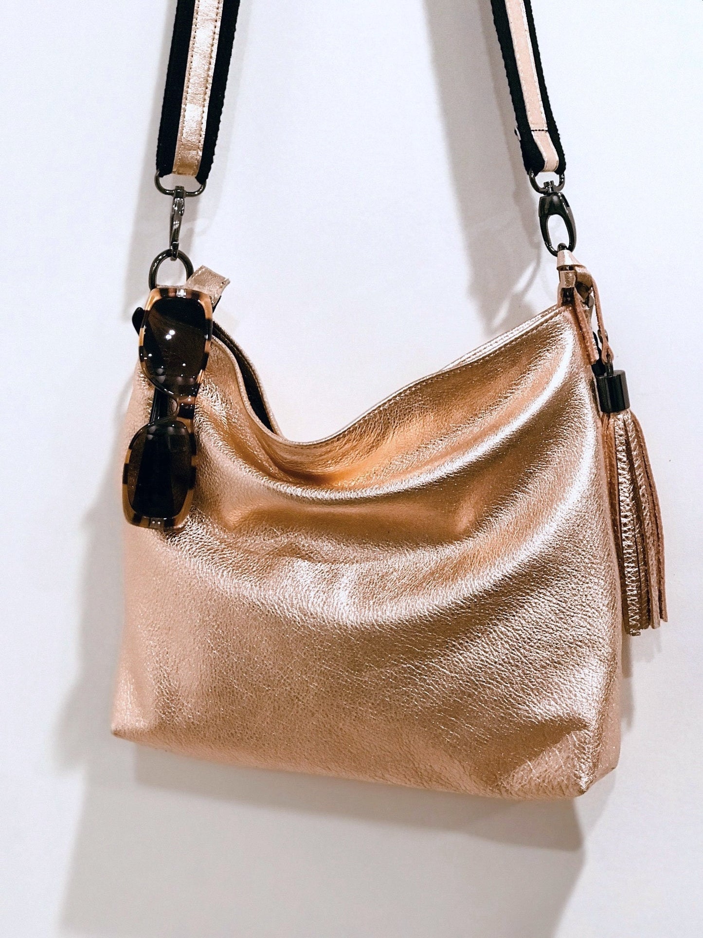 peach Gold metalli handbag with sunglasses hanging from top and a matching tassel with a black strap 