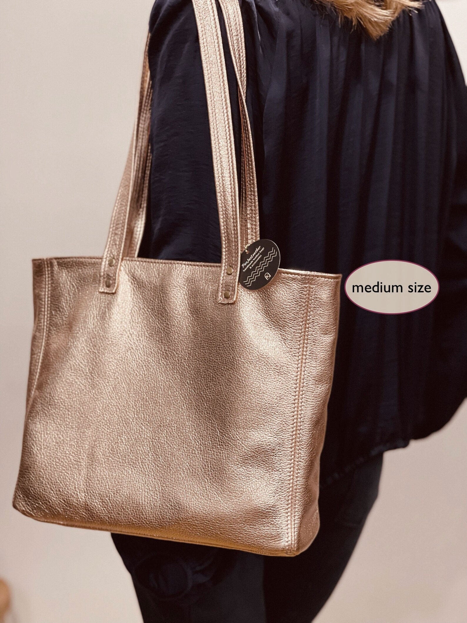 Rose gold metallic leather medium size  tote bag held by a person with a design label attached