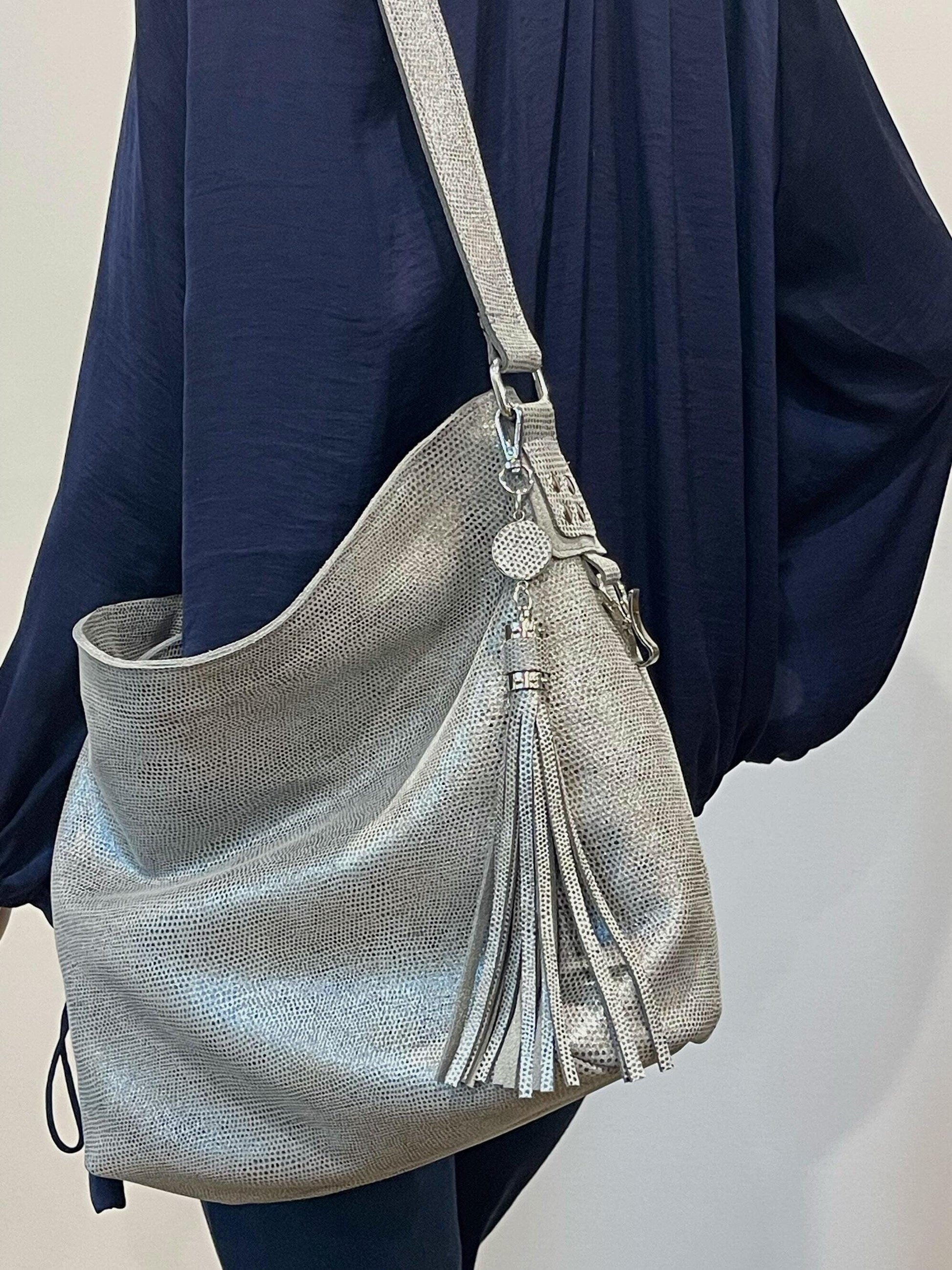 Silver textured handbag with tassel detail worn over a dark blue outfit