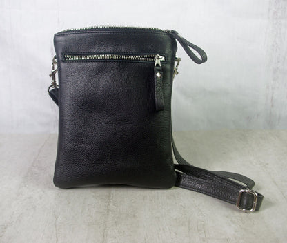 Black leather crossbody bag on a light gray surface with a white background