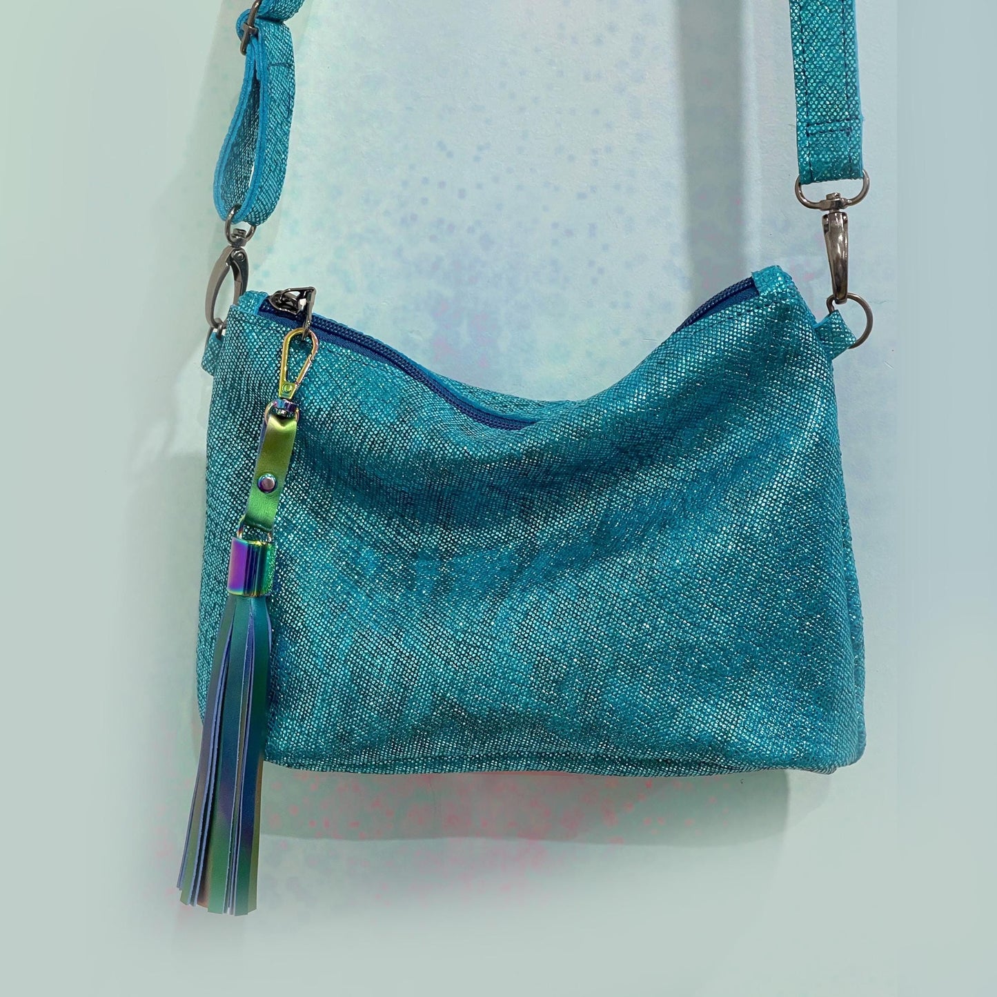 small pretty texture aqua teal handbag with a tassel on a light gray background