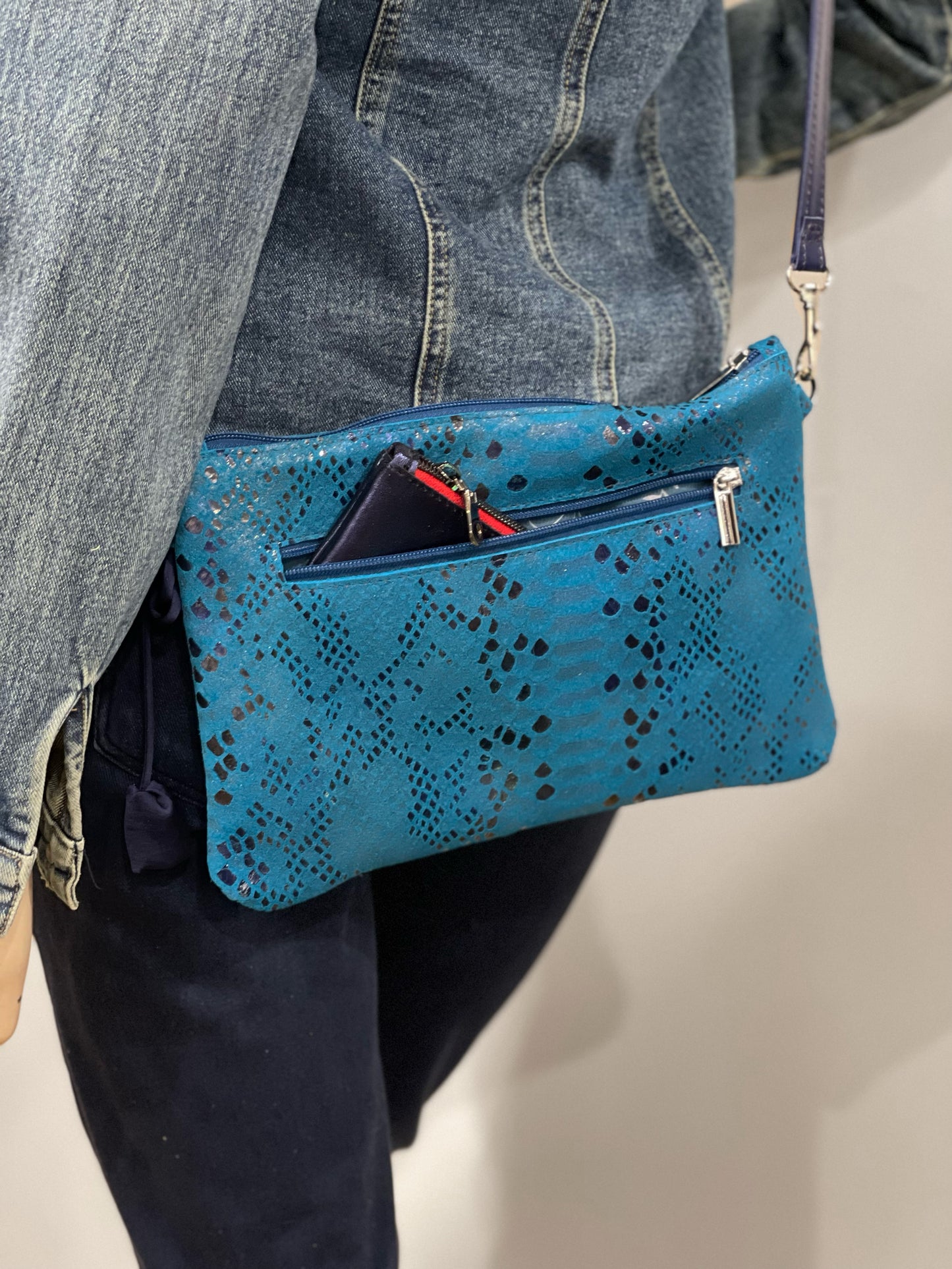 model wearing a crossbody snake embossed small blue leather bag with outside zipper pocket and showing a purse inside the pocket