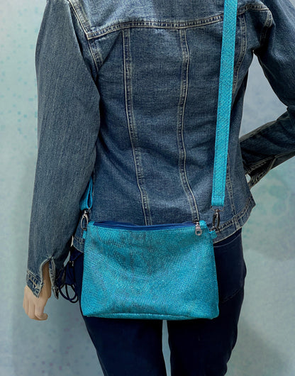 Person wearing a blue denim jacket with a matching teal textured surface and smooth to touch handbag on a light gray background