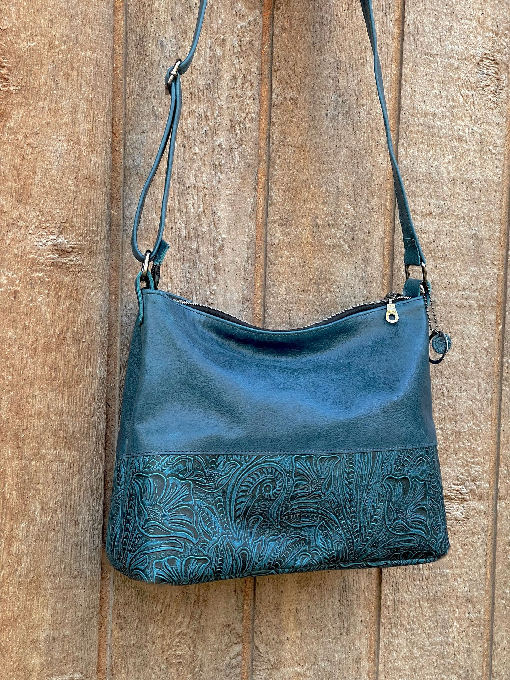 Teal Blue leather handbag with floral embossing on a wooden surface