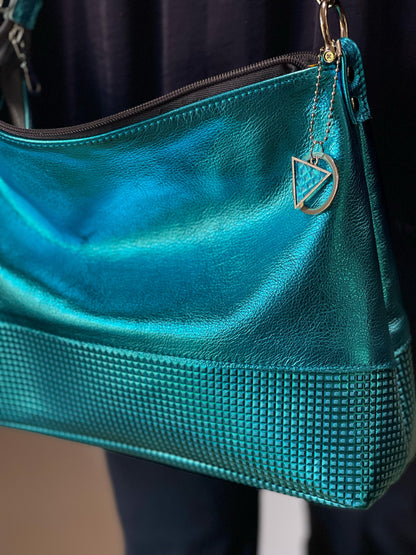 close up of Turquoise metal leather bag with lower half made from embossed tiny squares. a handmade metal and leather charm attached to bag.