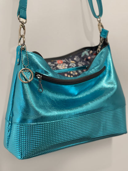 turquoise Blue shiny metal handbag with floral interior on a light gray background