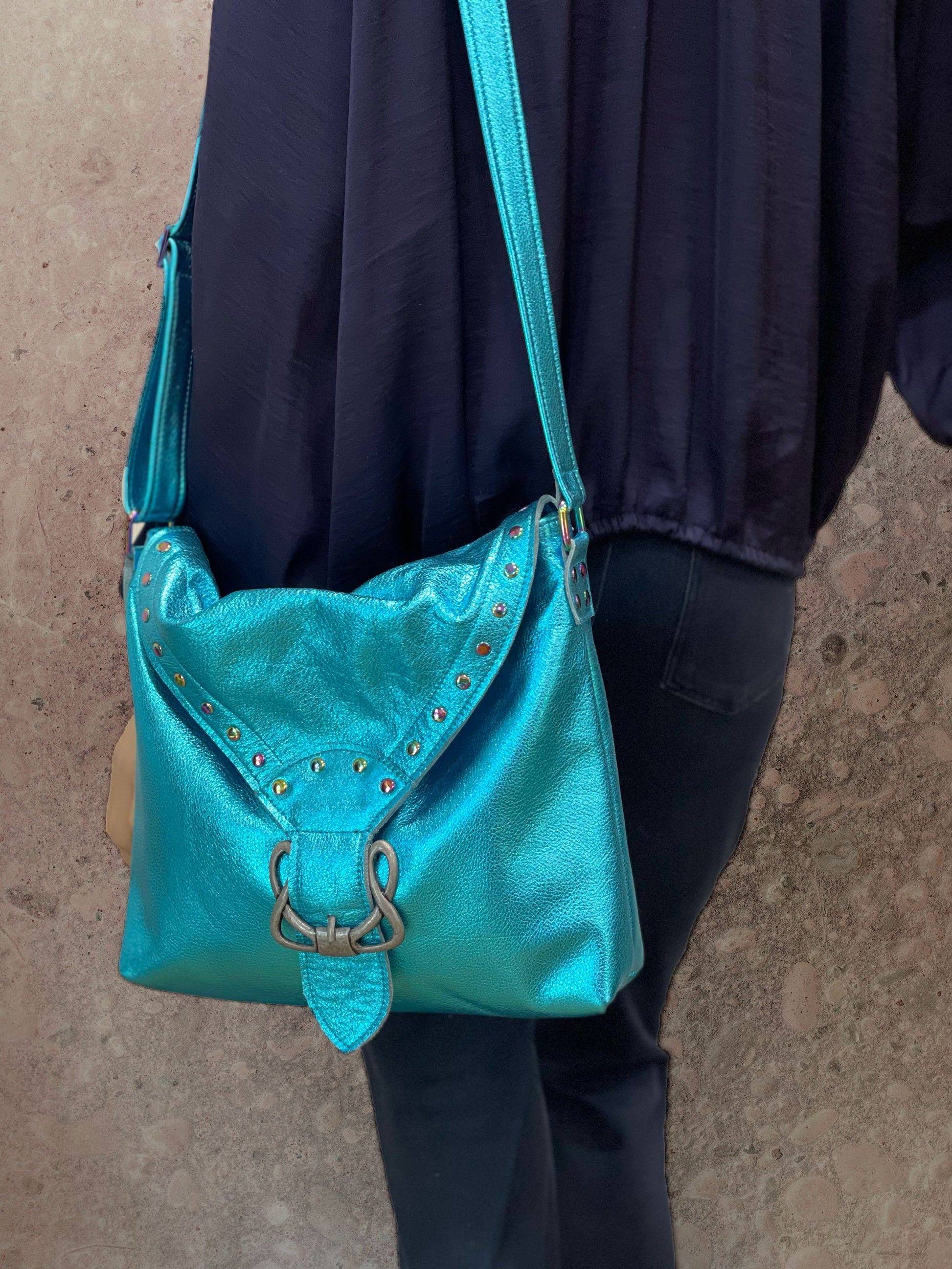 Turquoise handbag with decorative studs and celtic style buckle held by a person against a neutral background