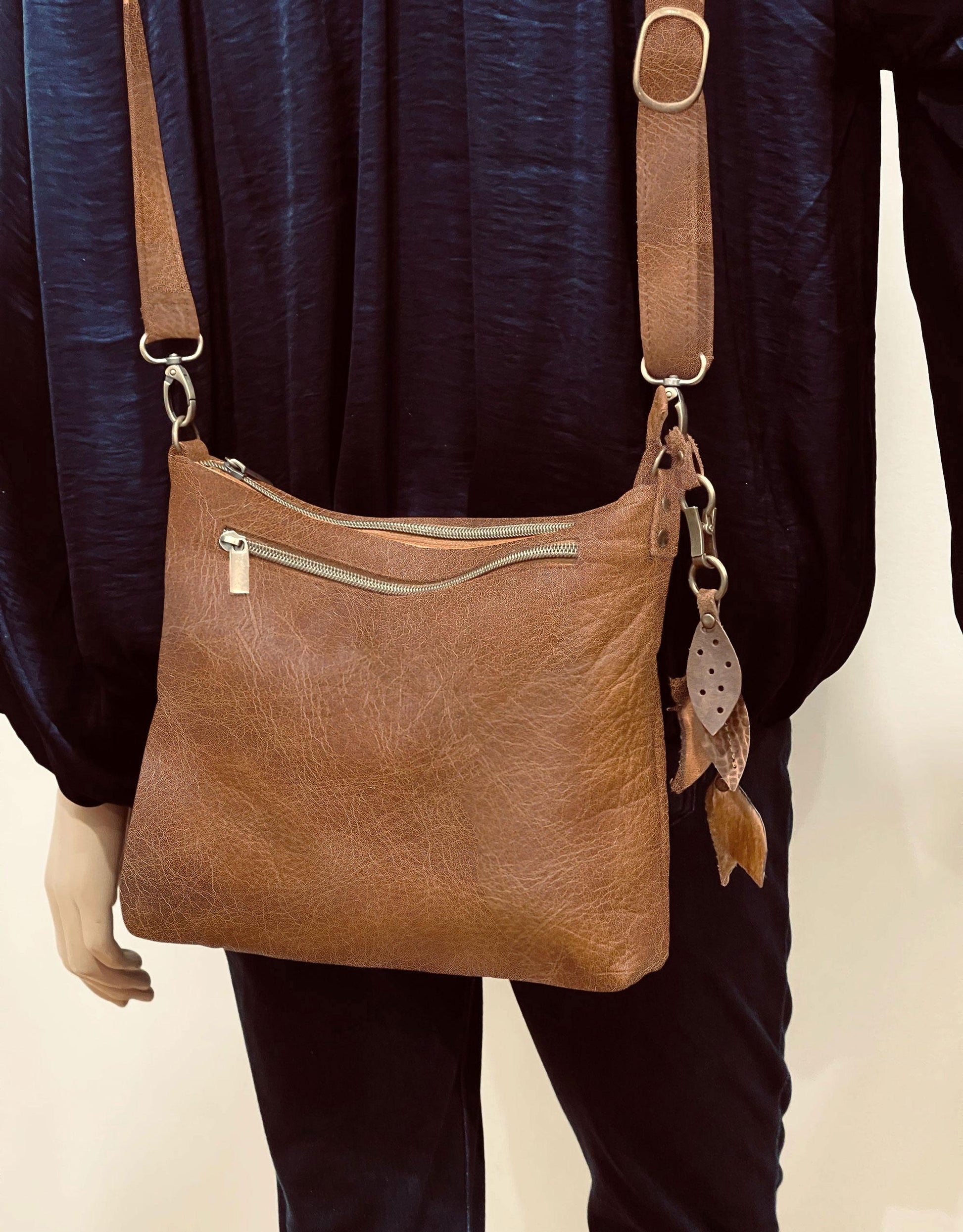 Brown leather shoulder bag with decorative elements worn by a person against a neutral background