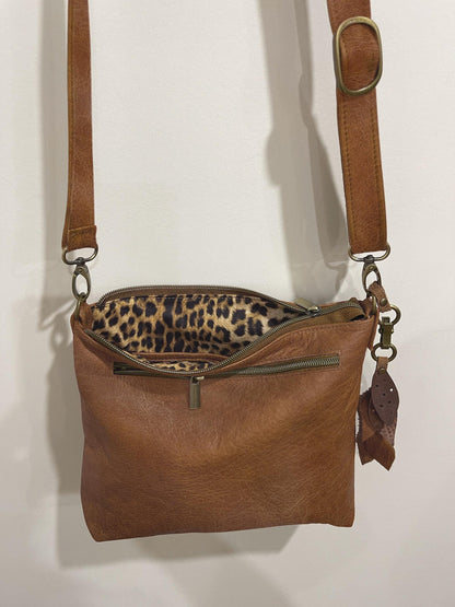 Brown leather handbag with leopard print interior on a white background