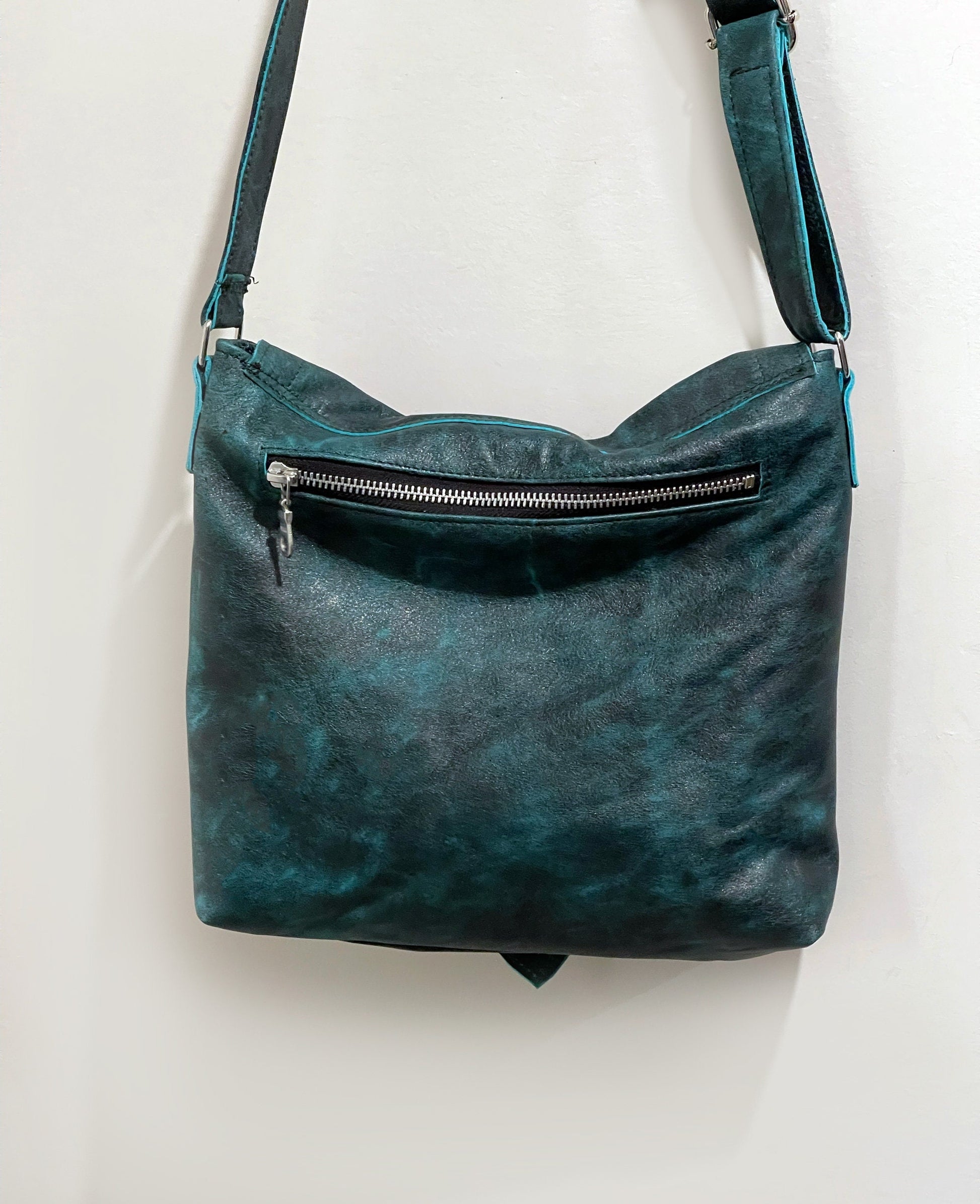 Teal leather handbag with a visible silver zipper on a white background