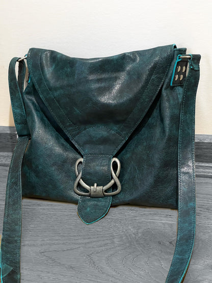 Teal leather handbag with silver buckle on a wooden surface